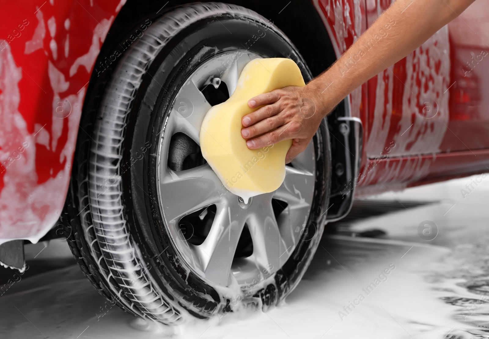 Photo of Man washing red auto with sponge at car wash, closeup