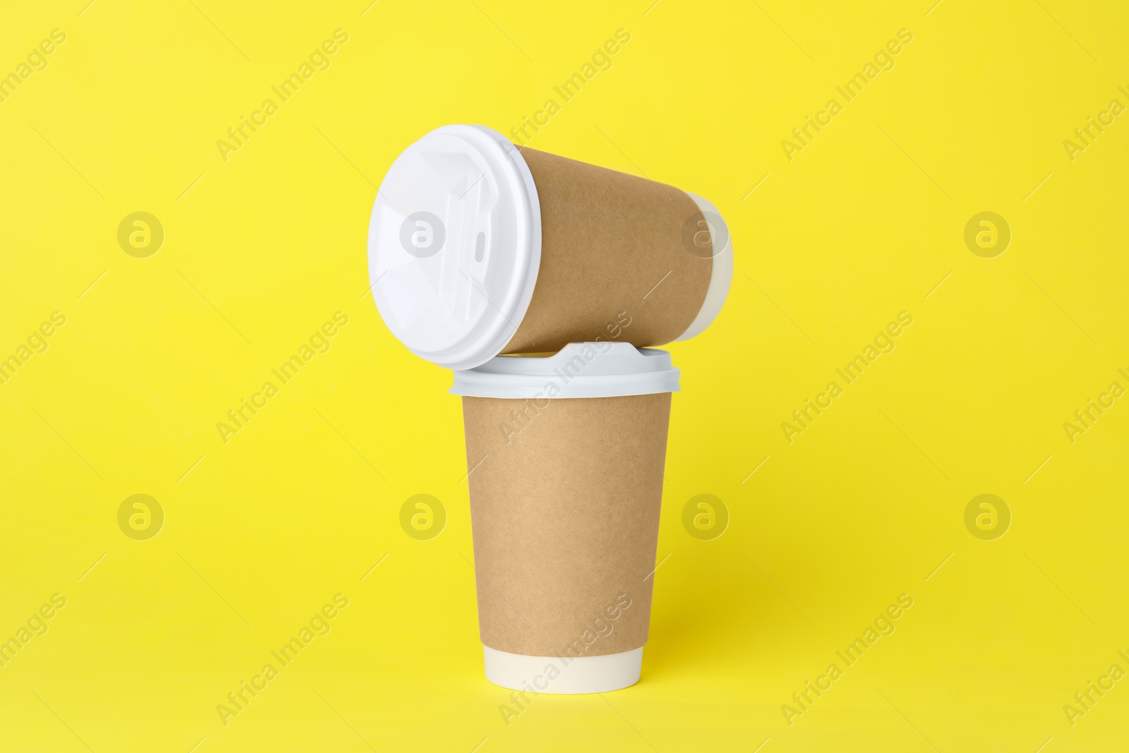 Photo of Paper cups with white lids on yellow background. Coffee to go