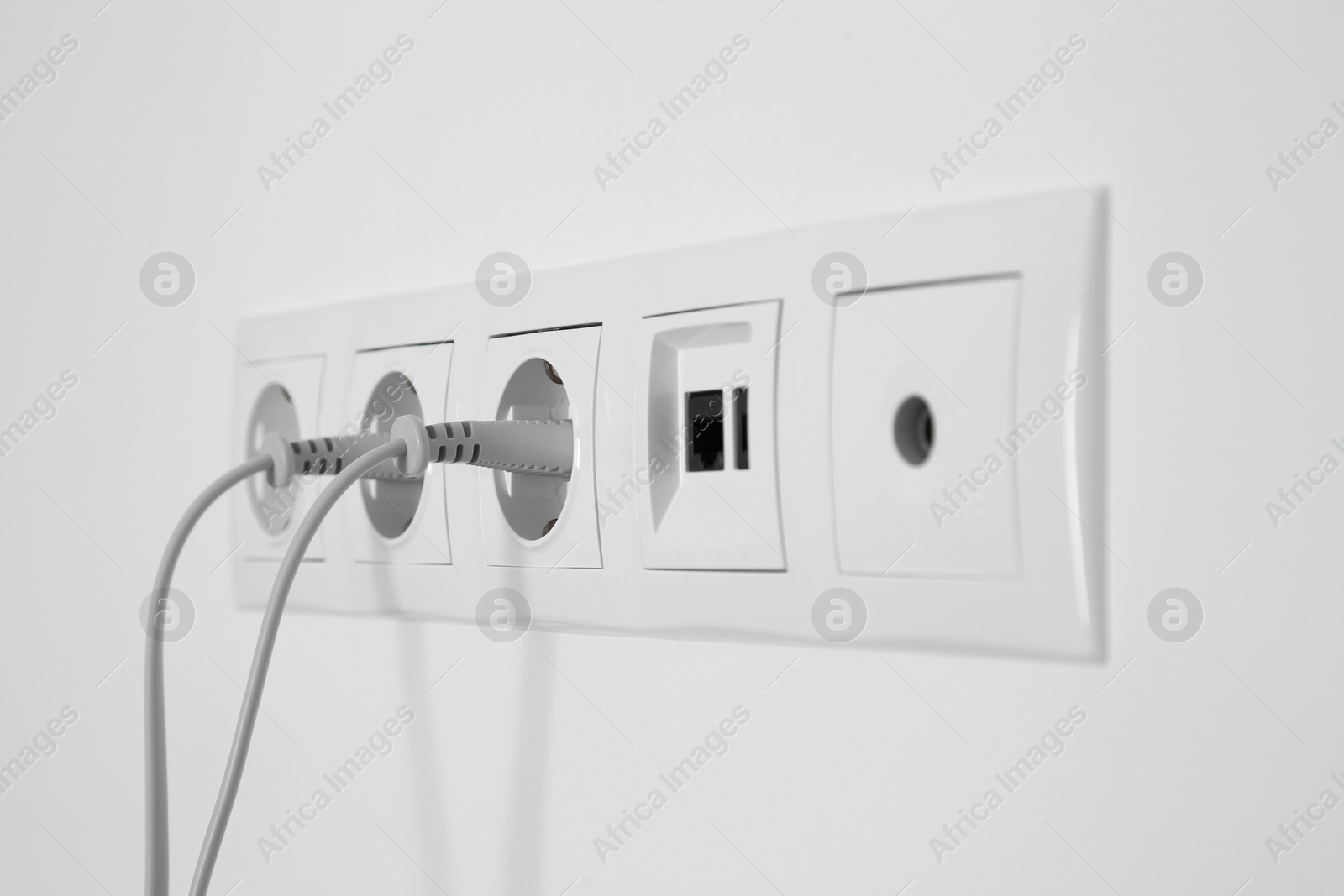 Photo of Many power sockets with plugs, ethernet and TV coax plates on white wall indoors