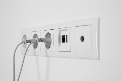 Many power sockets with plugs, ethernet and TV coax plates on white wall indoors