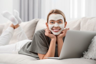 Photo of Young woman with face mask using laptop on sofa at home. Spa treatments