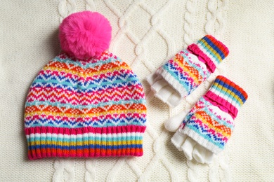 Warm hat and mittens on white knitted fabric, flat lay