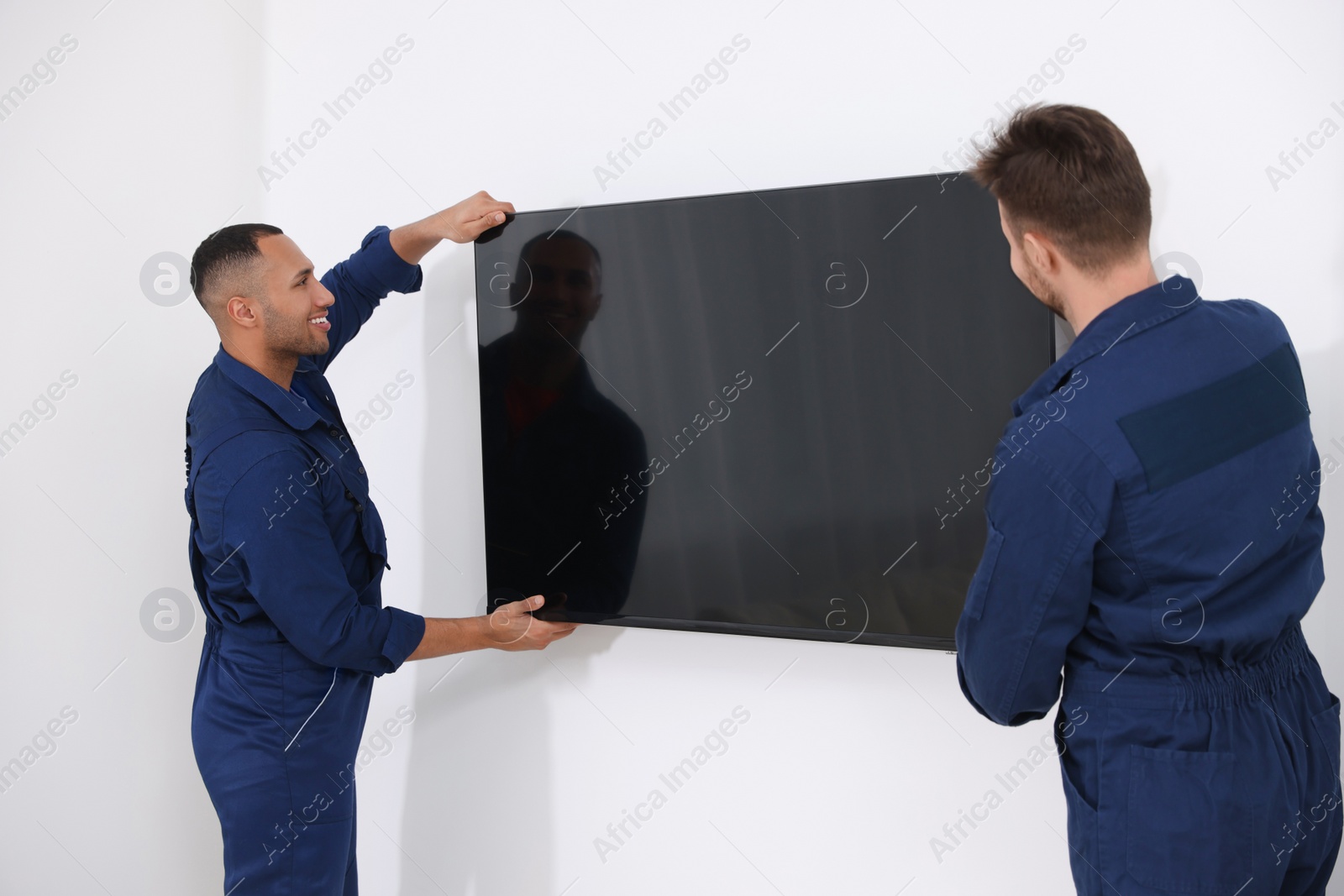 Photo of Male movers carrying plasma TV near white wall indoors