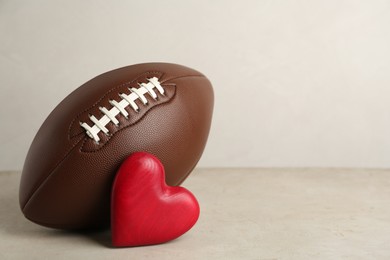 Photo of American football ball and heart on light grey table against white background. Space for text