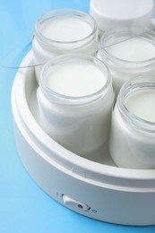Photo of Modern yogurt maker with full jars on light blue background, closeup