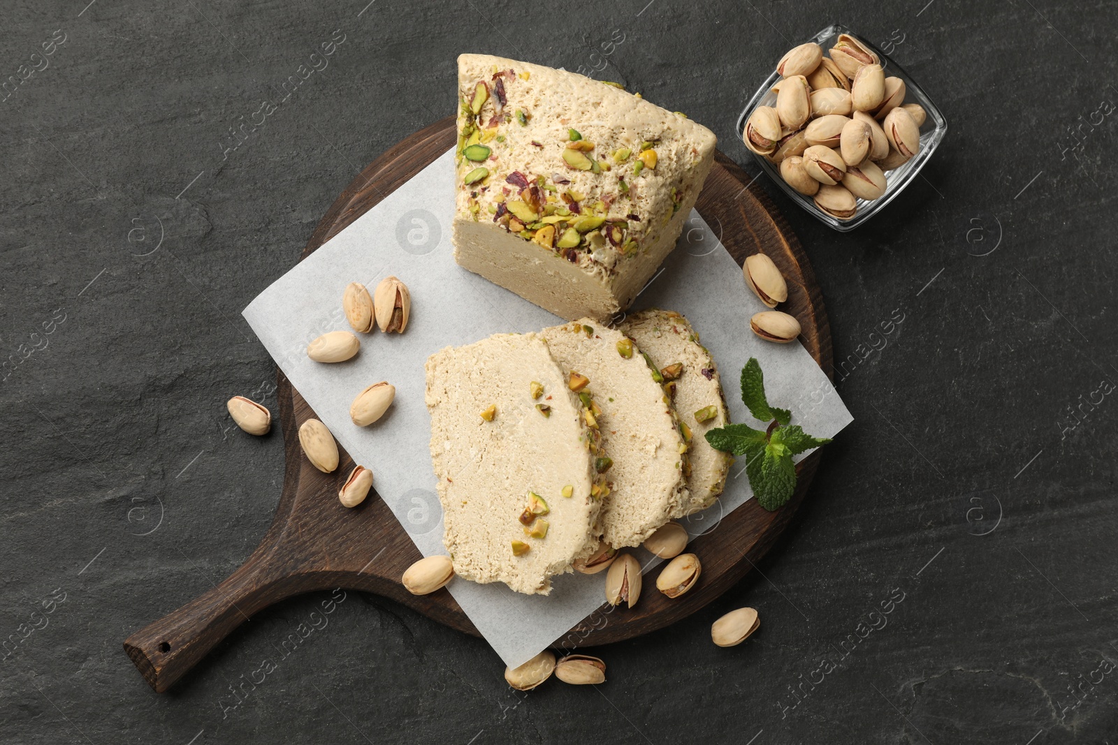 Photo of Tasty halva with pistachios and mint on grey table, top view