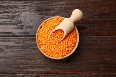 Photo of Raw red lentils and scoop in bowl on wooden table, top view