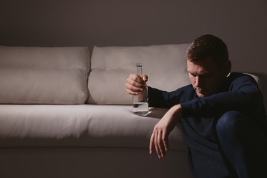 Addicted man with alcoholic drink near sofa indoors. Space for text