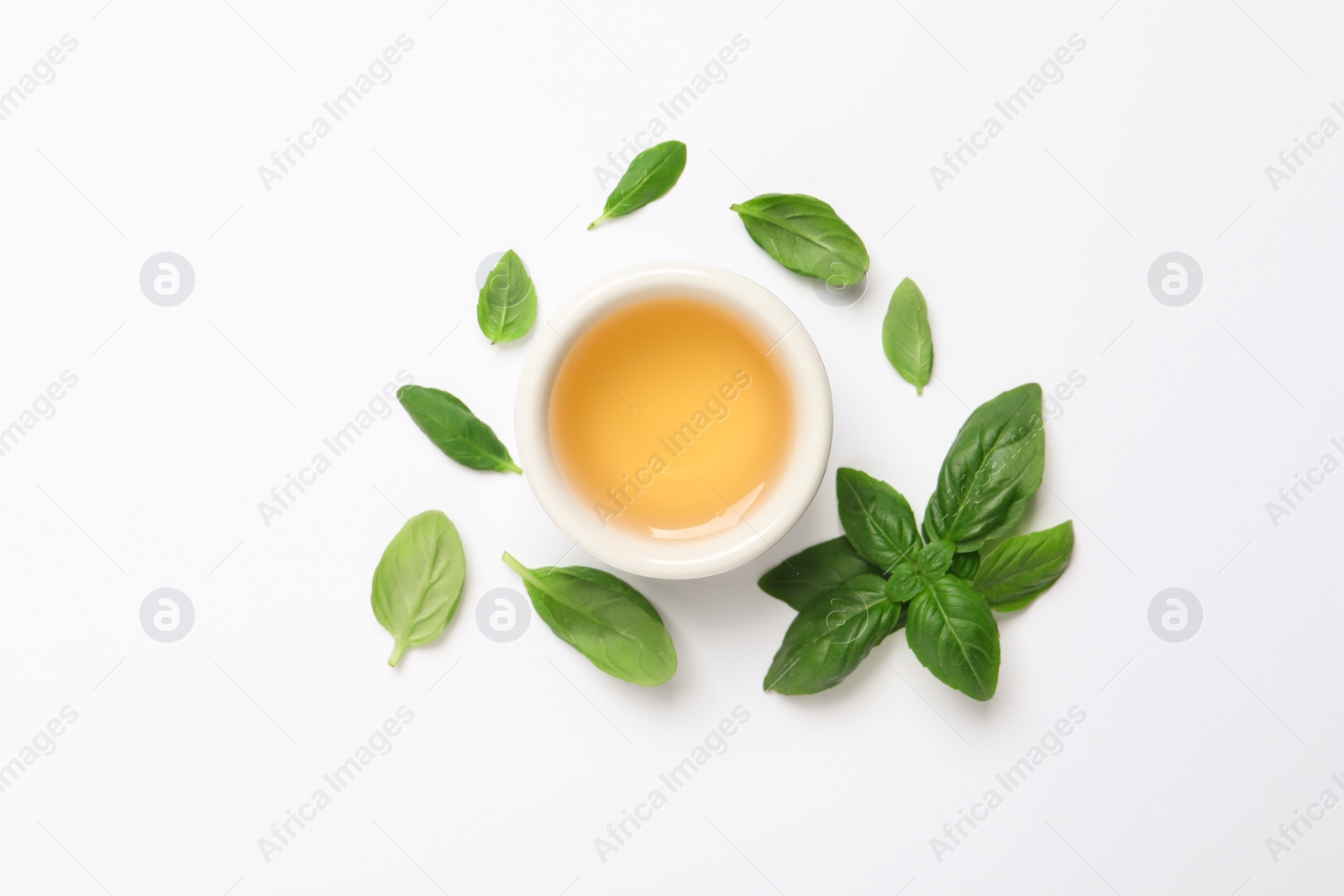 Photo of Essential basil oil and fresh leaves on white background, flat lay