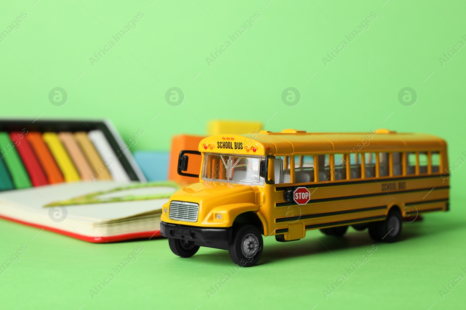 Photo of School bus model and stationery on green background. Transport for students