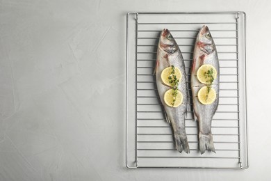 Photo of Oven rack with raw sea bass fish, lemon and thyme on light grey table, top view. Space for text