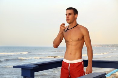 Handsome lifeguard with whistle on watch tower near sea