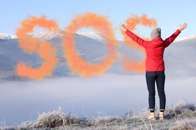 Image of Woman and word SOS made of color smoke bomb in mountains, back view