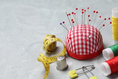 Photo of Checkered pincushion with pins and other sewing tools on grey table