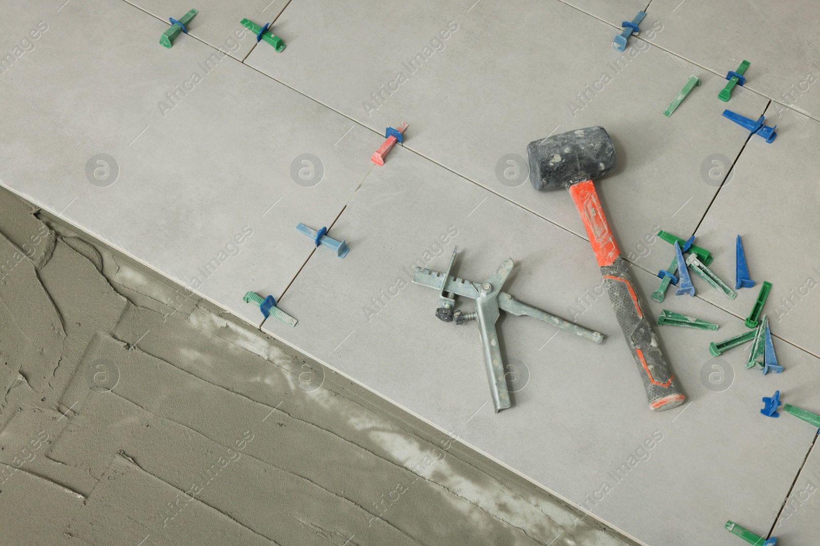 Photo of Beautiful tiles with colorful wedges and professional equipment near adhesive mix on floor, top view