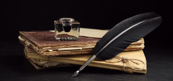 Image of Quill, inkwell and old books on black table. Banner design