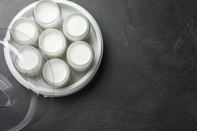 Photo of Modern yogurt maker with full jars on dark grey table, top view. Space for text