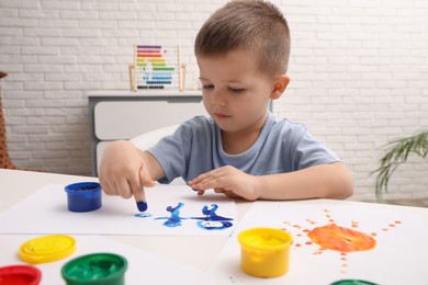 Photo of Little boy painting with finger at white table in room