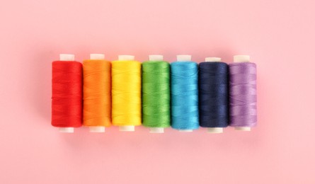 Photo of Different sewing threads on pink background, flat lay