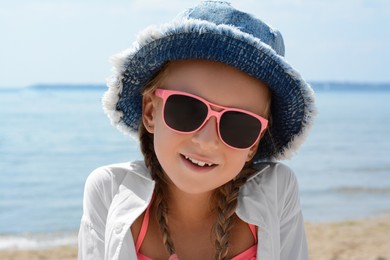Little girl wearing sunglasses and hat at beach on sunny day