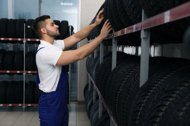 Male mechanic near rack with car tires in auto store