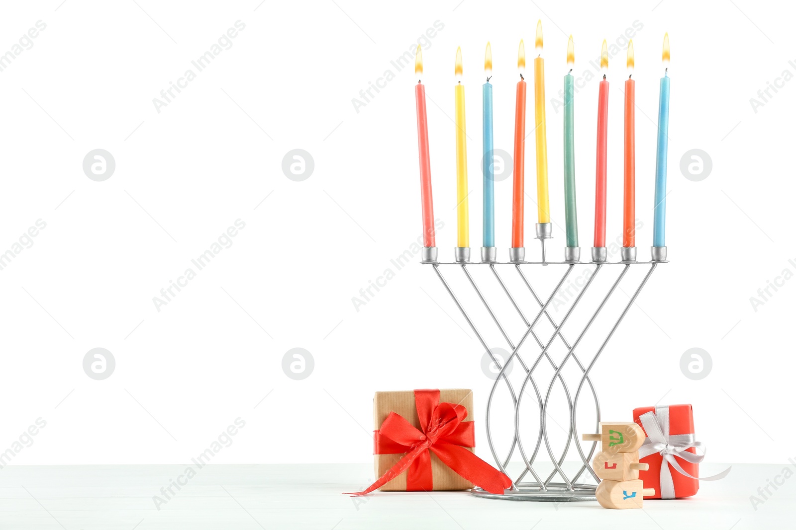 Photo of Hanukkah celebration. Menorah with colorful candles, dreidels and gift boxes on white background