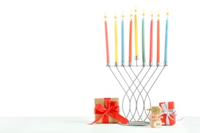 Photo of Hanukkah celebration. Menorah with colorful candles, dreidels and gift boxes on white background