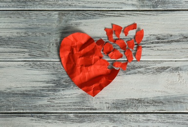 Photo of Crumpled red paper heart with torn away pieces on wooden background, top view