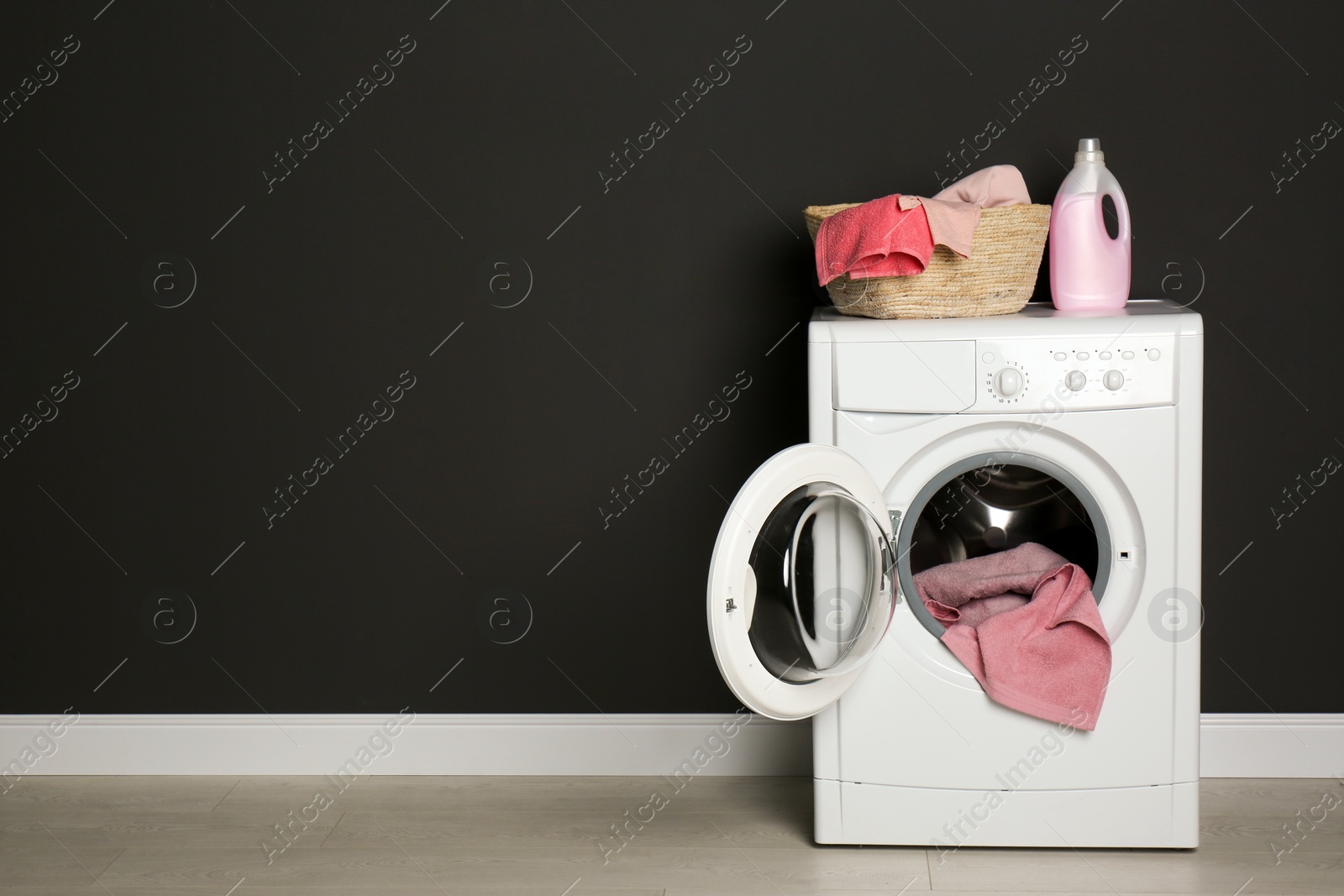 Photo of Modern washing machine with laundry, wicker basket and detergent near black wall. Space for text