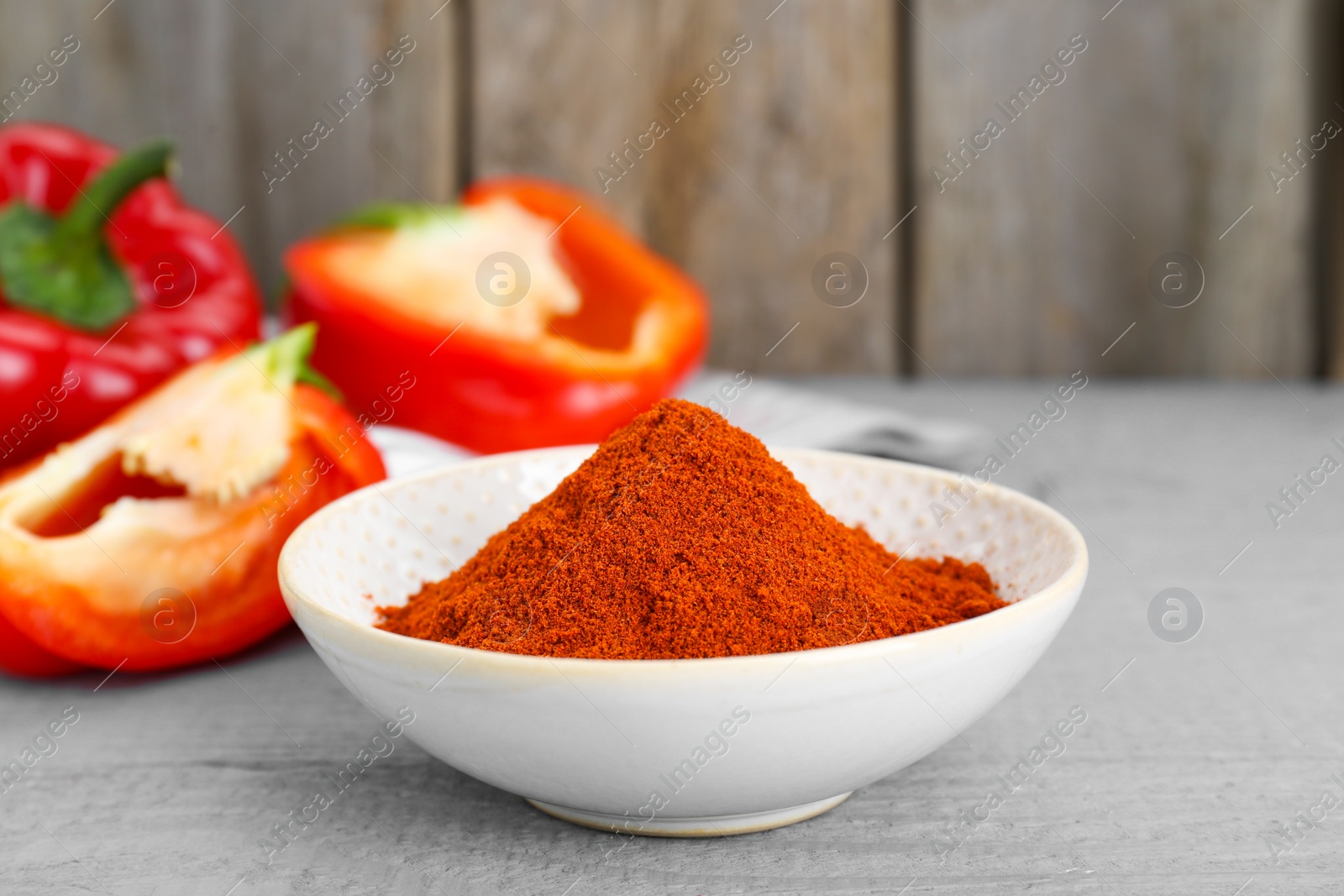 Photo of Bowl with aromatic paprika powder and fresh bell peppers on grey wooden table