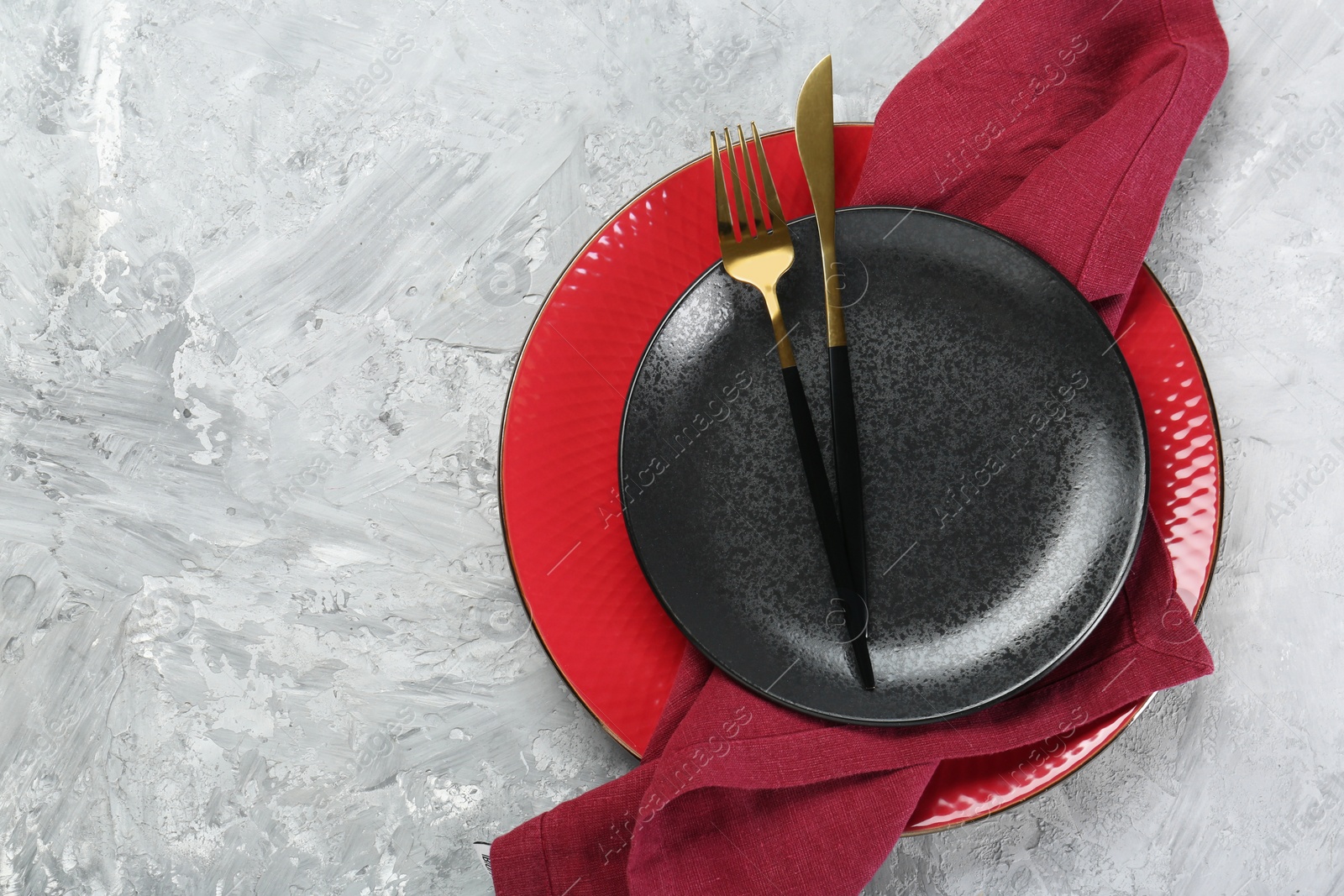 Photo of Clean plates, cutlery and napkin on gray textured table, top view. Space for text