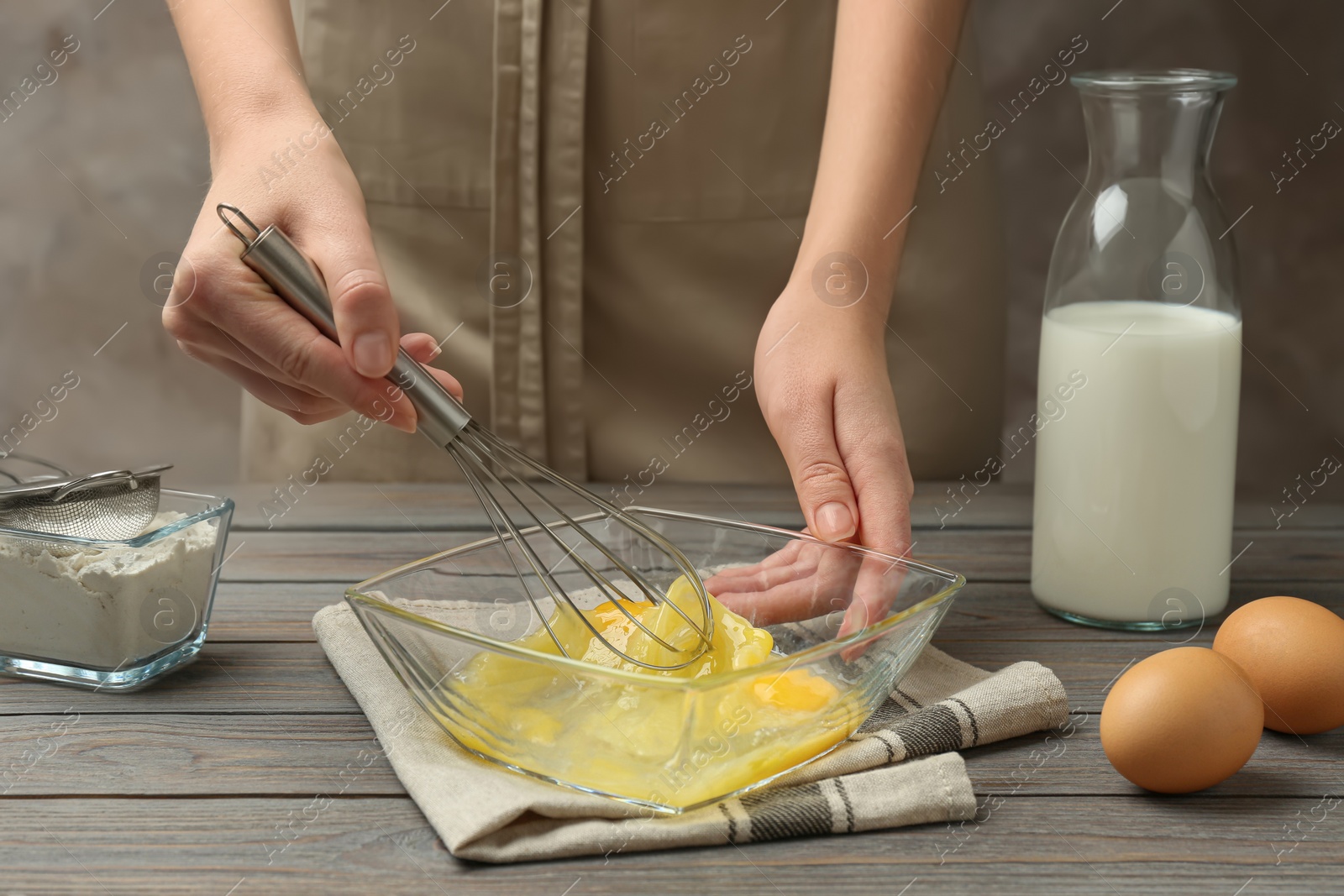 Photo of Woman whisking eggs in glass bowl at wooden table, closeup