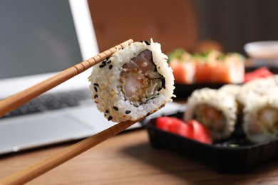 Photo of Holding sushi roll with chopsticks over table, closeup