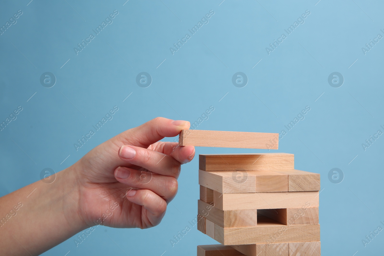 Photo of Woman playing Jenga on light blue background, closeup. Space for text