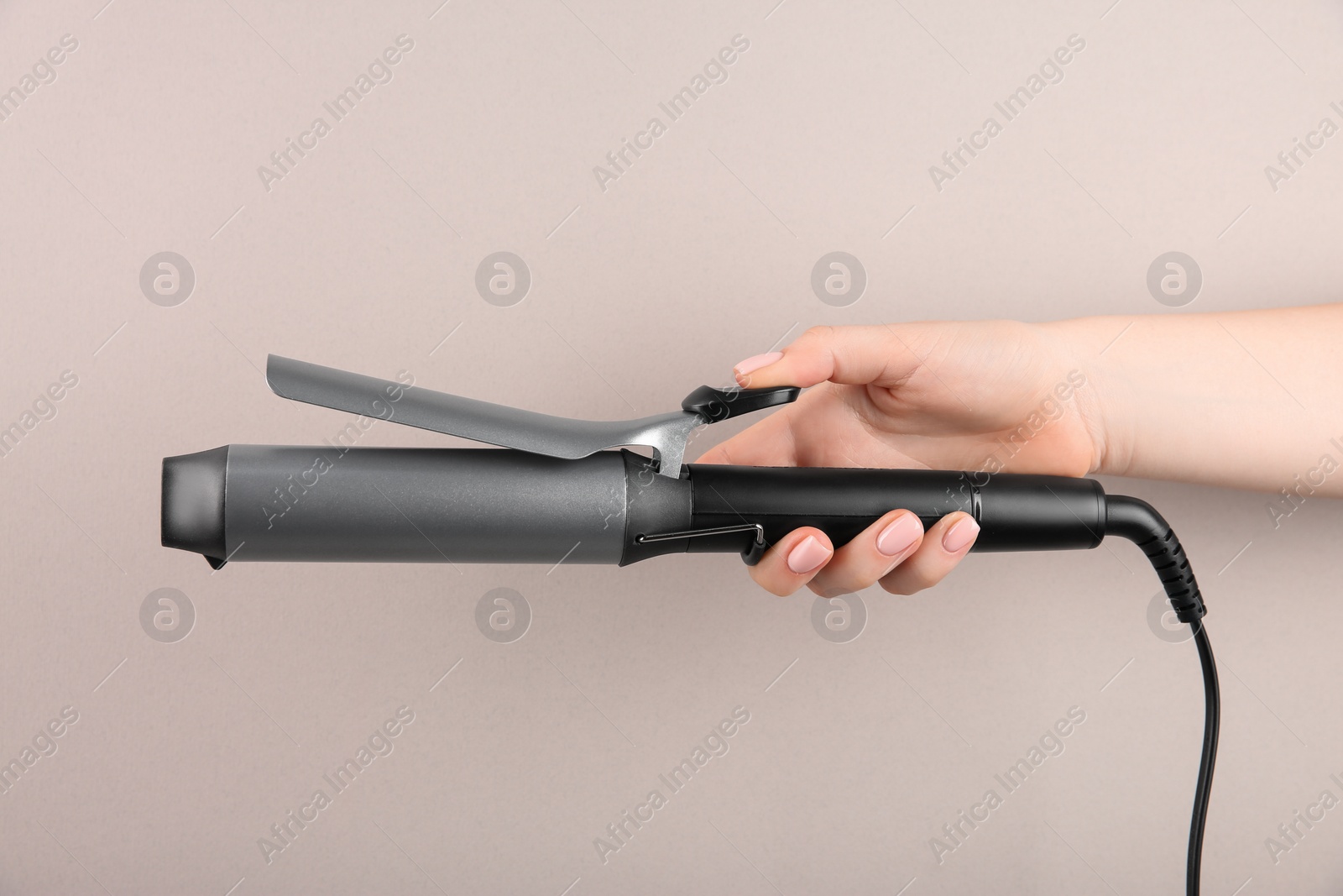 Photo of Hair styling appliance. Woman holding curling iron on light grey background, closeup
