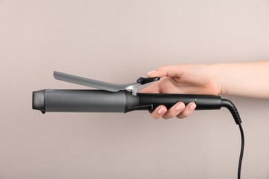 Photo of Hair styling appliance. Woman holding curling iron on light grey background, closeup