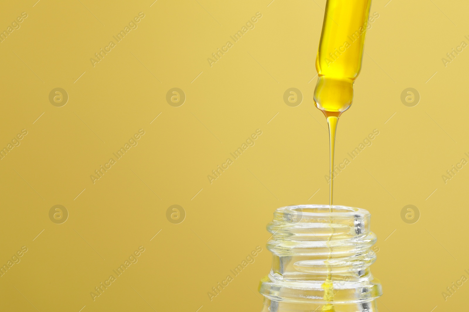 Photo of Dripping serum from pipette into bottle on yellow background, closeup. Space for text