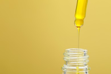 Photo of Dripping serum from pipette into bottle on yellow background, closeup. Space for text