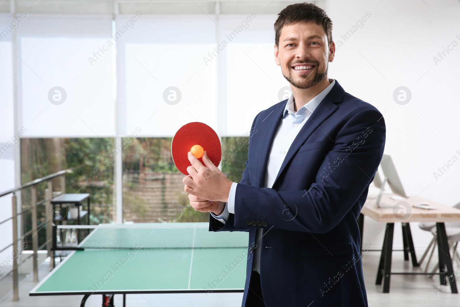 Photo of Businessman with tennis racket and ball near ping pong table in office