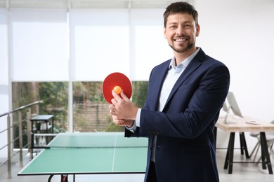 Photo of Businessman with tennis racket and ball near ping pong table in office