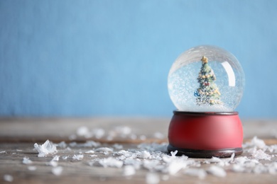 Magical snow globe with Christmas tree on wooden table against color background. Space for text