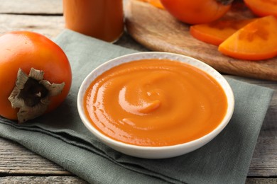 Photo of Delicious persimmon jam and fresh fruits on wooden table