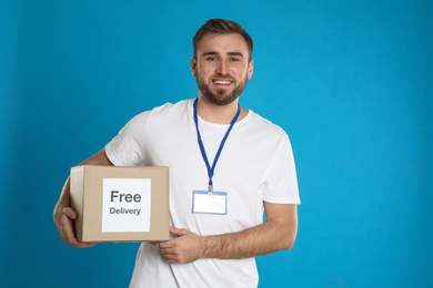 Photo of Male courier holding parcel with sticker Free Delivery on light blue background