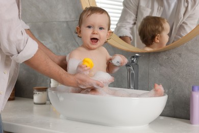 Father washing his little baby in sink at home