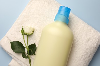 Photo of Bottle of fabric softener, terry towel and beautiful rose on light background, top view