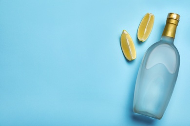 Photo of Bottle of vodka and lemon on light blue background, flat lay. Space for text