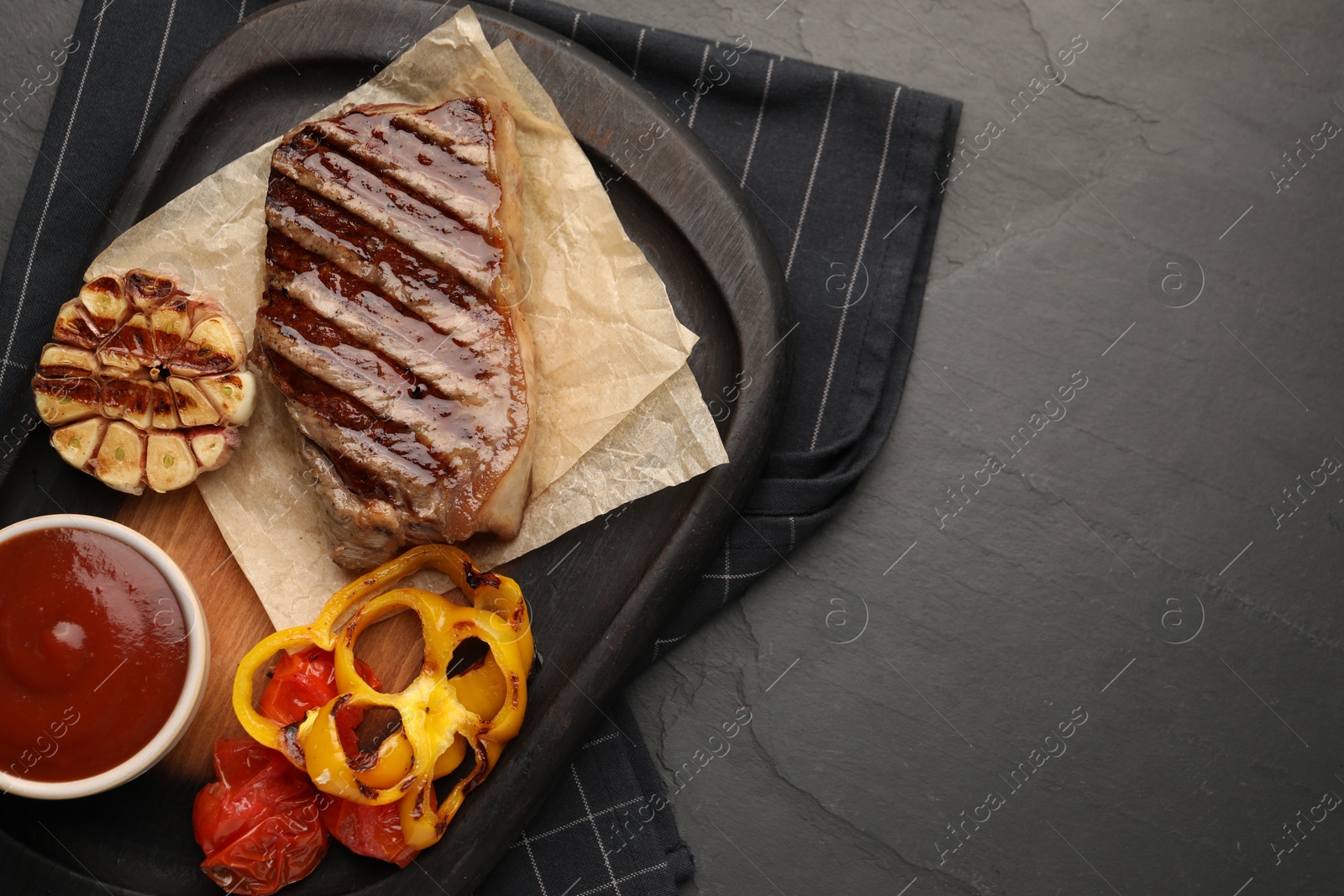 Photo of Delicious grilled beef steak with spices and tomato sauce on dark gray table, top view. Space for text