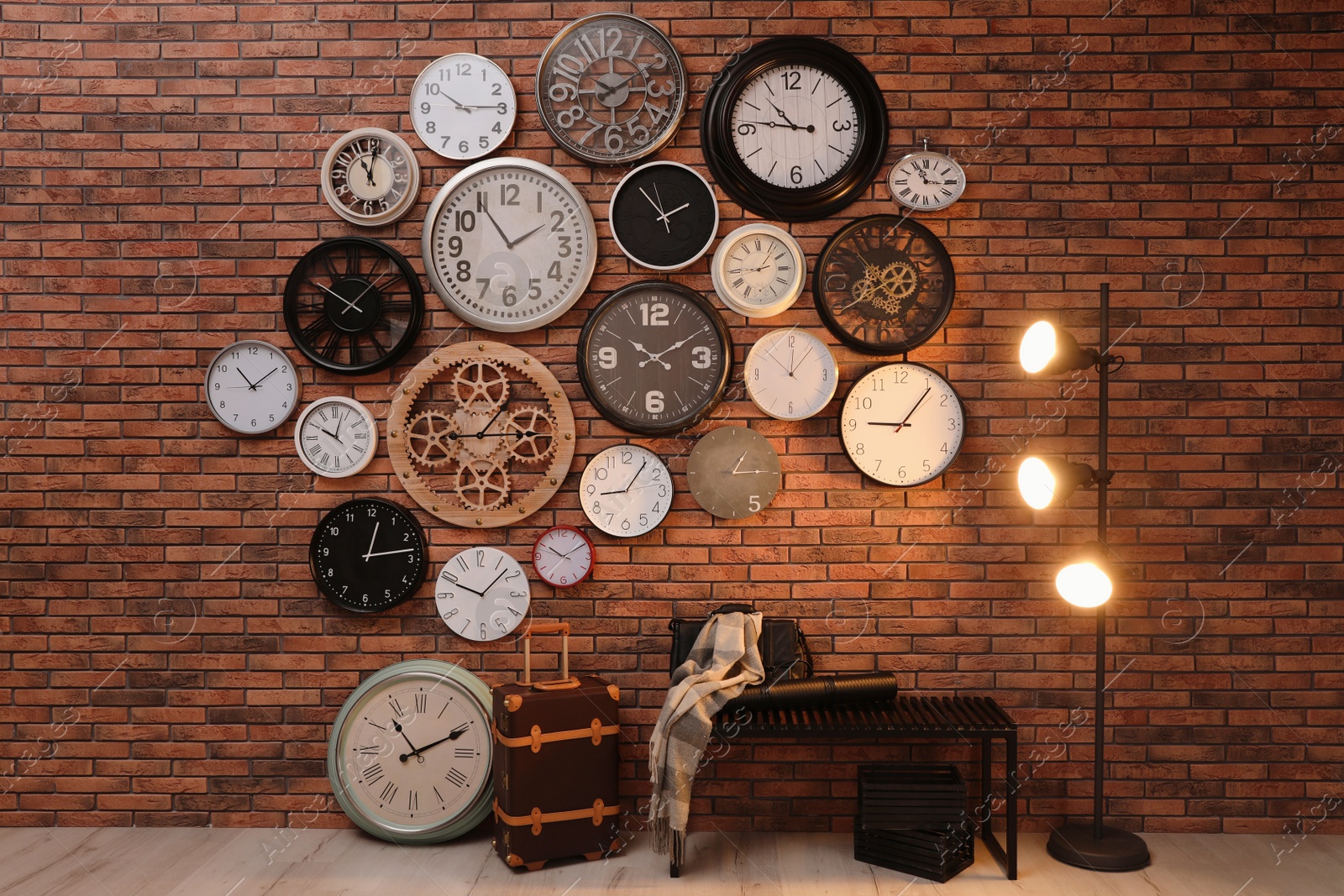 Photo of Collection of clocks hanging on red brick wall indoors