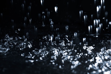 Photo of Heavy rain falling down on ground against dark background, closeup