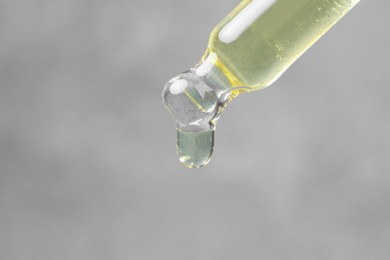 Photo of Dripping cosmetic oil from pipette on grey background, macro view